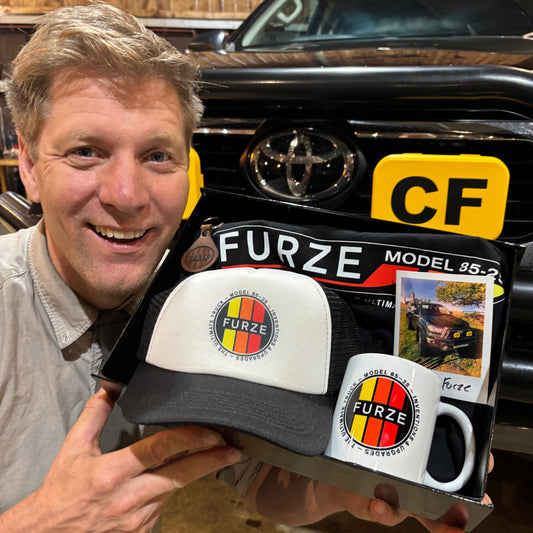 Colin Furze holding the Trucker 2025 Bundle merch with his Toyota Hilux in the background