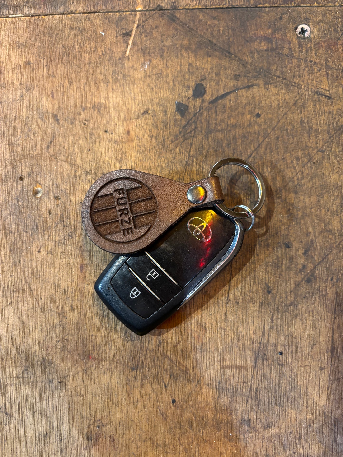 Brown leather keychain with 'FURZE' branding on a car key fob against a wooden background
