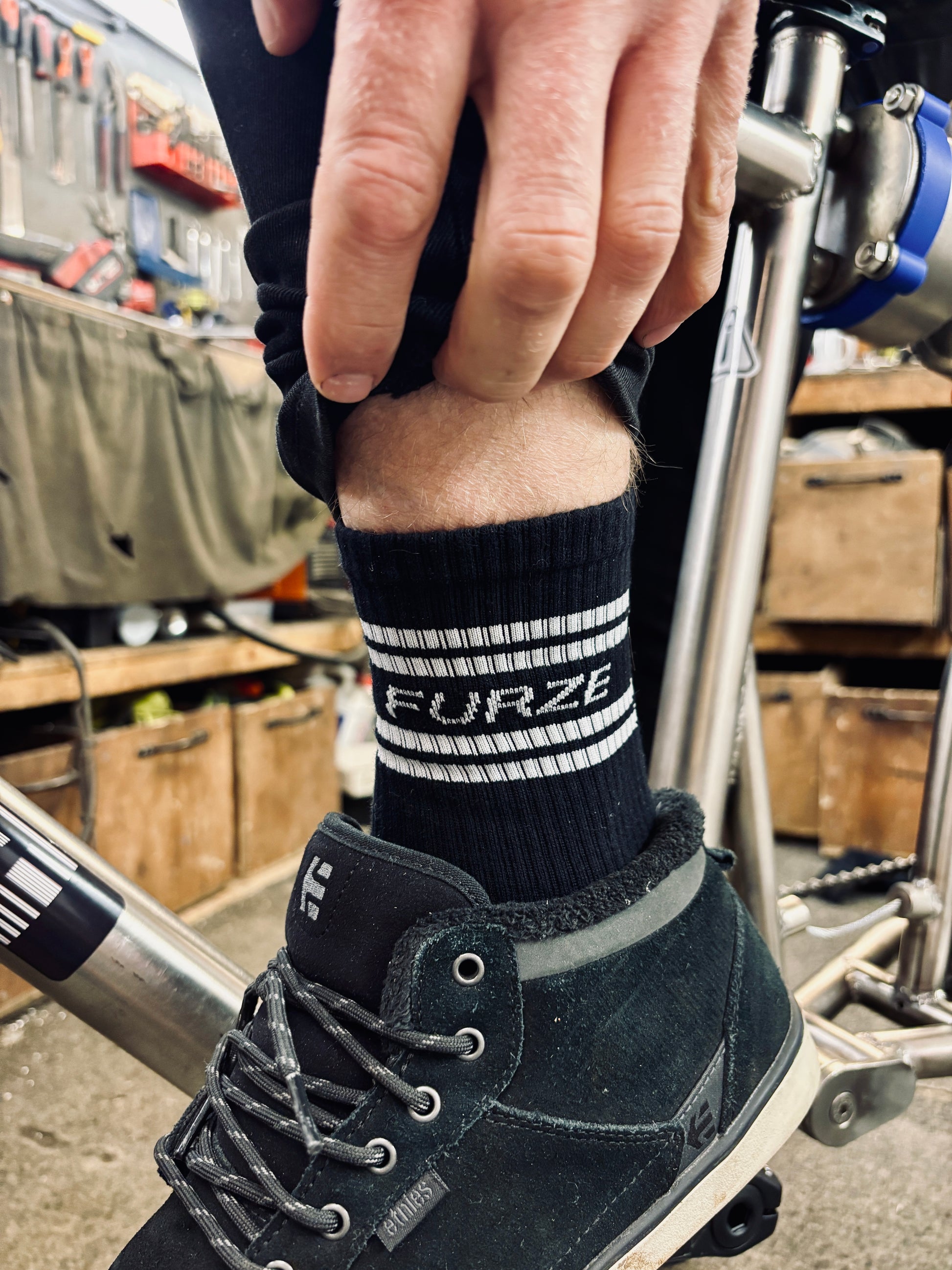 Close up of Colin's ankle sporting 'FURZE' branding on his sock with the workshop in the background